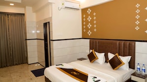 A hotel room with a neatly made bed, a bedside table with a water bottle, and an air conditioning unit mounted on the wall. - MAJESTIC INN (Vasai)