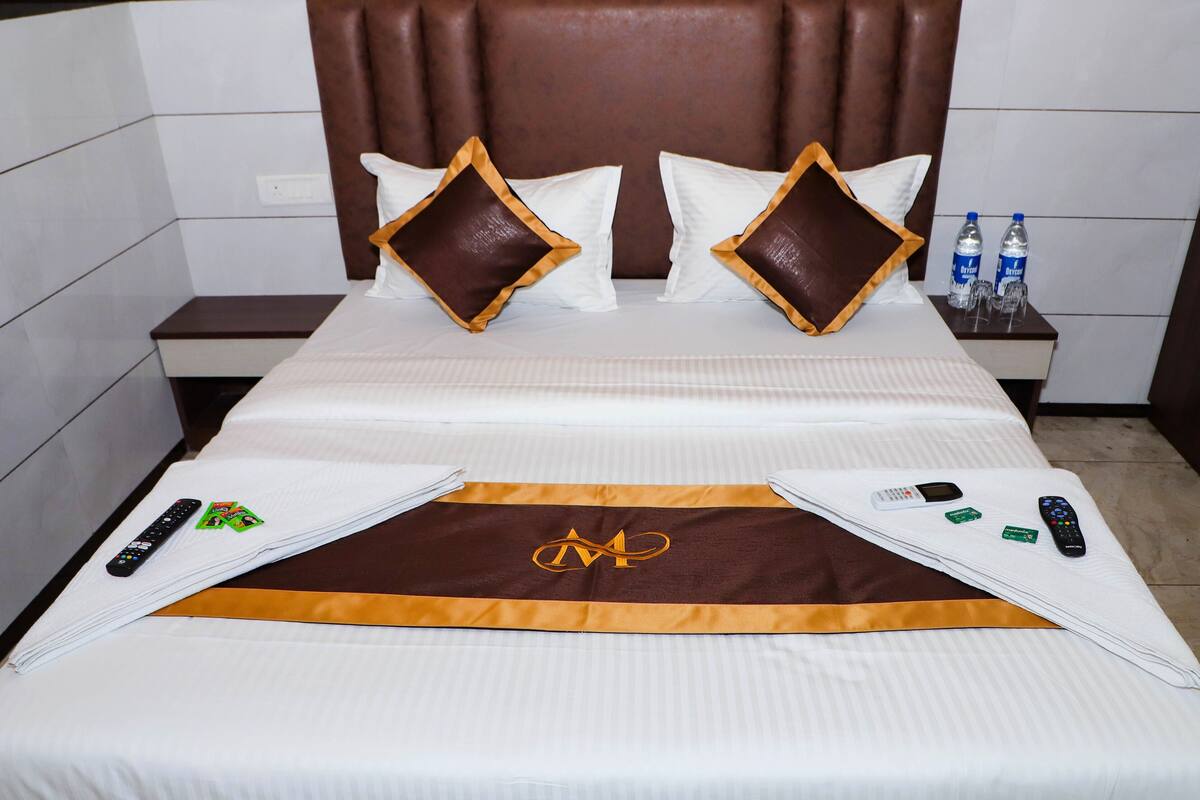 A hotel room with a bed, pillows, a nightstand, and two remote controls.