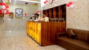 A reception area with a wooden counter, a brown sofa, and a ceiling fan. - MAJESTIC INN (Vasai)