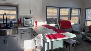 A modern kitchen with white cabinets, a stainless steel refrigerator, and a built-in oven. There are two windows providing natural light and a view of the outside. - If you”re looking for that perfect weekend get away, you just found it! (Fries)