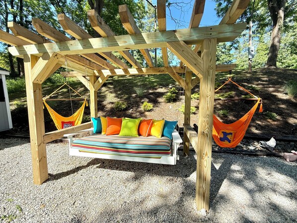 Puinen pergola, jossa on riippukeinu ja värikkäillä tyynyillä varustettu keinutuoli.