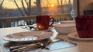 A dining table with plates, cups, and cutlery, set against a window with a view of bare trees and a sunset. - If you”re looking for that perfect weekend get away, you just found it! (Fries)