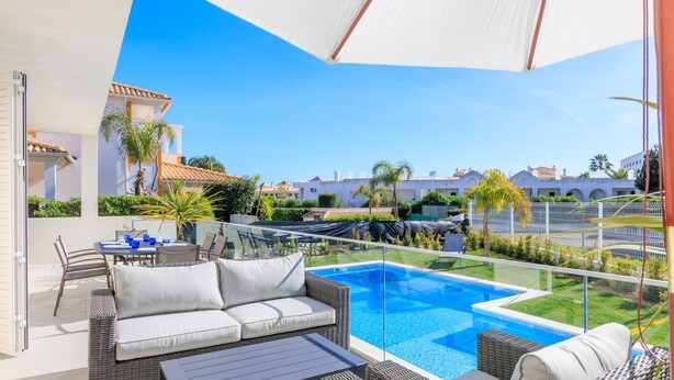 Área de piscina no terraço, com guarda-corpo de vidro, mobiliário de exterior e vista para edifícios vizinhos.