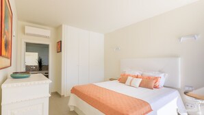 Quarto com cama, guarda-roupa branco e uma pequena mesa com espelho.