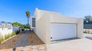 Uma casa moderna com porta de garagem branca, um caminho de acesso de cascalho e uma palmeira.