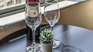 Une table avec une bouteille de vin et deux verres, une petite plante, et une vue sur un paysage urbain par la fenêtre.