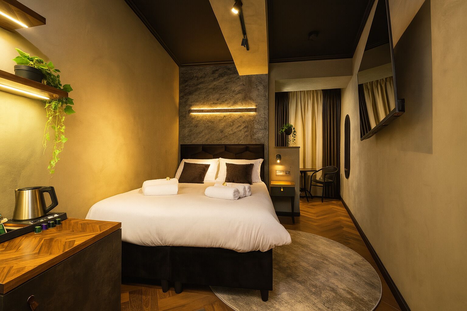 A modern hotel room with a large bed, bedside tables, a coffee machine, and a small desk.