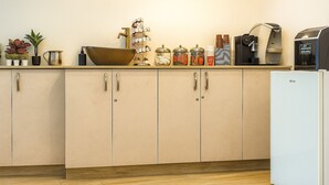 Une cuisine avec des armoires de couleur beige, un évier, une machine à café et divers ustensiles de cuisine disposés sur le plan de travail.