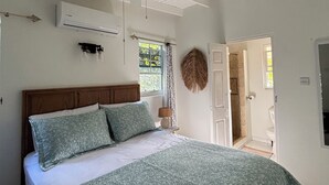 A bedroom with a bed, ceiling fan, air conditioning unit, and a view of the outside.
