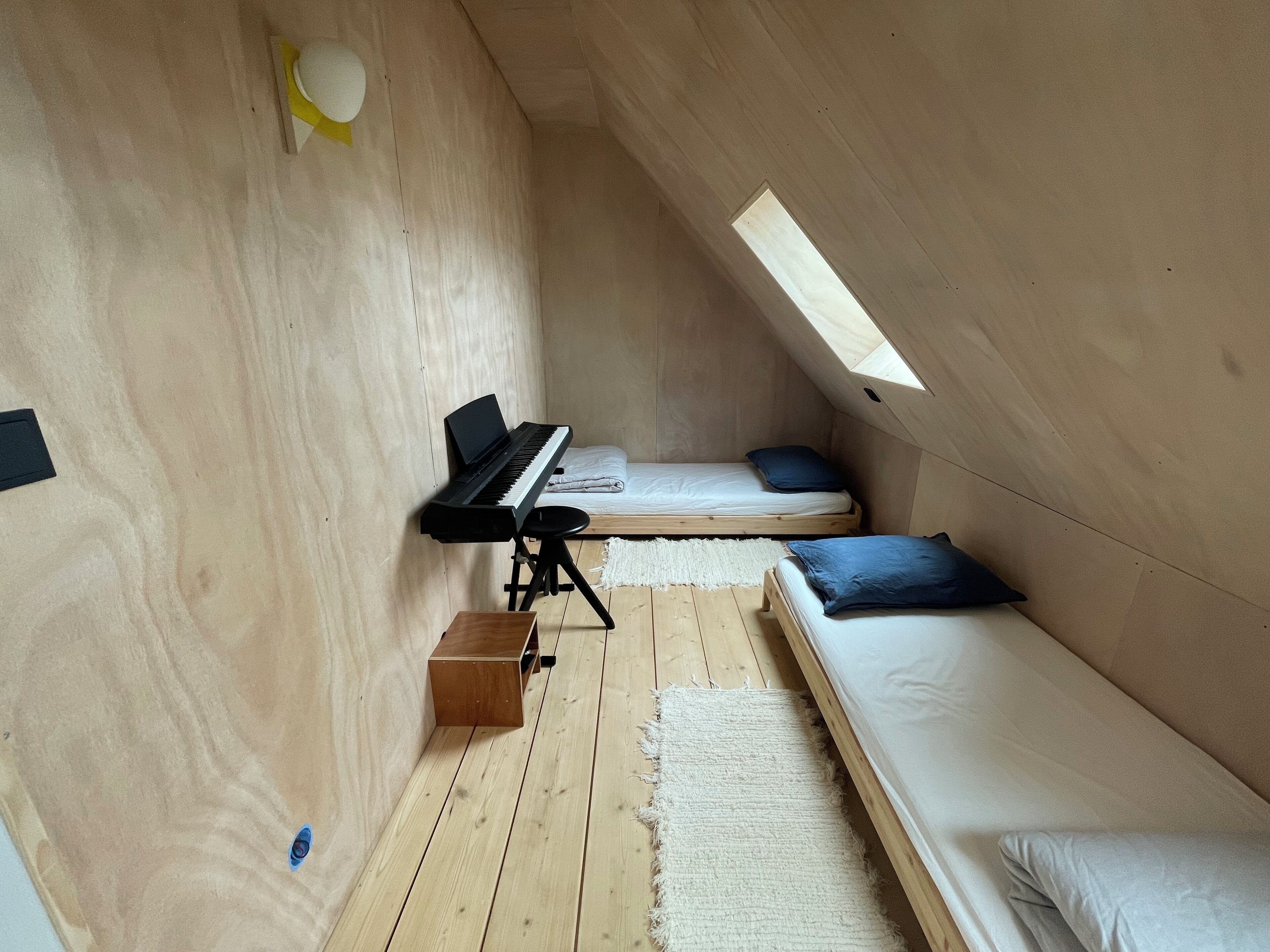 Ein gemütliches Dachzimmer mit Klavier, zwei Betten und einem Oberlicht.