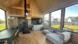 Ein modernes Interieur mit Essbereich, Küche und Sitzgelegenheit, gekennzeichnet durch große Fenster und Holzarchitektur.