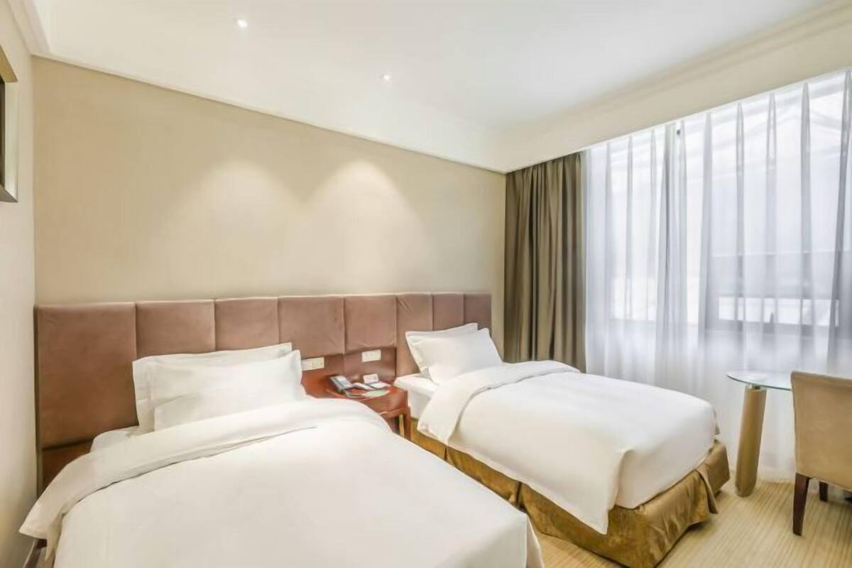 Quarto de hotel com duas camas, uma mesinha e uma cadeira.