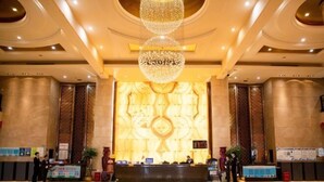 Un hall d’entrée spacieux, doté d’un comptoir de réception, d’un grand lustre et d’un mur orné d’un motif décoratif situé derrière le comptoir.