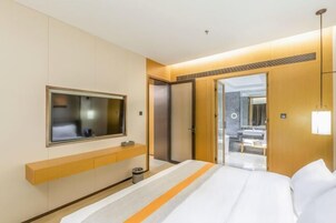 Habitación de hotel con una cama, televisor, espejo, aparador de madera y una puerta que da a un baño.