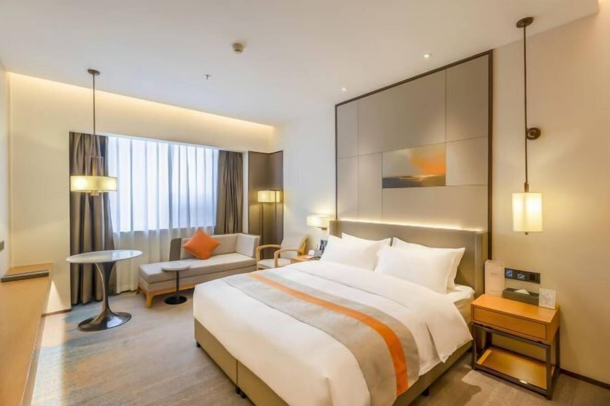 Quarto de hotel com uma cama grande, um sofá, uma mesinha e uma mesa de cabeceira.