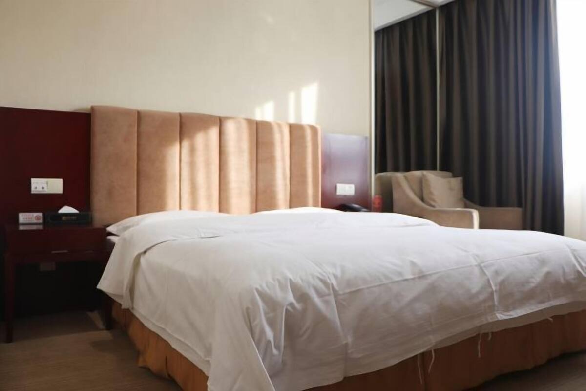 Quarto de hotel com uma cama grande, cabeceira de madeira, uma escrivaninha com telefone e uma cadeira.