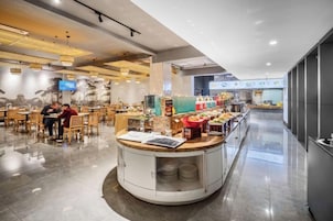 Un restaurante moderno con una barra central, mesas para comer y una barra alargada con exhibición de alimentos.