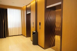 Habitación de hotel con paneles de madera, un bote de basura y una ventana con cortinas.