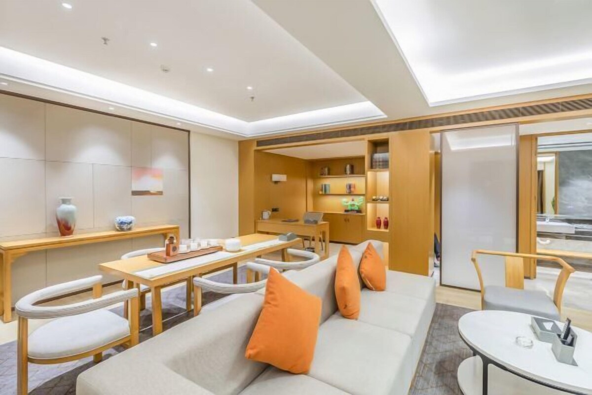 Una habitación de hotel moderna con sofá, mesa de comedor, sillas y una pequeña cocina.