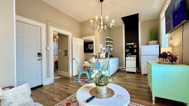 Una cocina moderna con armarios blancos, un comedor con una mesa redonda y una sala de estar con un sofá y una mesa de centro.