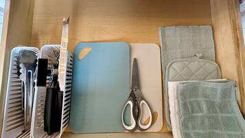 Eine Schublade mit einer blauen Unterlage, einer Schere, einem Messer mit schwarzem Griff, einer weißen Tablettgarnitur und einer grünen gesteppten Tasche.