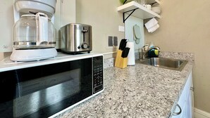Una cocina con cafetera, tostadora, microondas y un estante con cristalería.