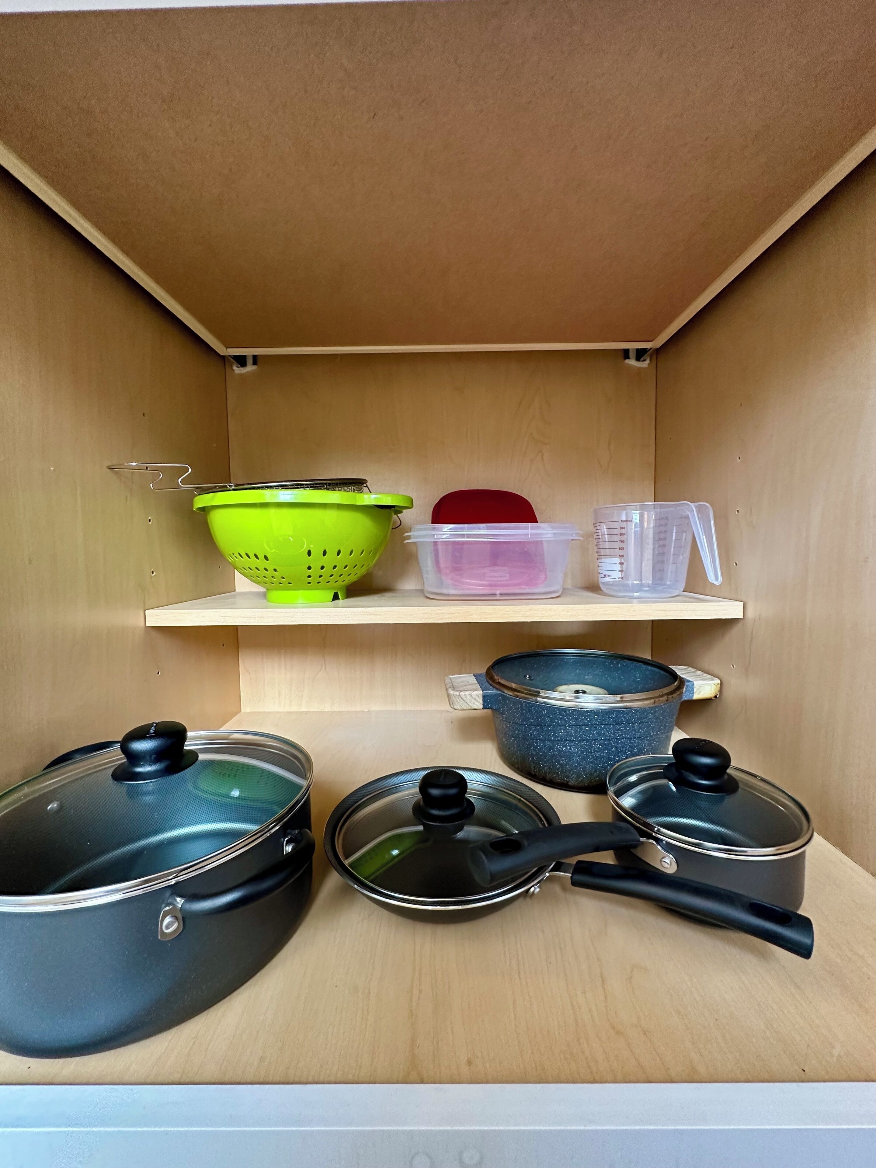 A kitchen with wooden cabinets, a shelf with kitchen utensils, and pots.