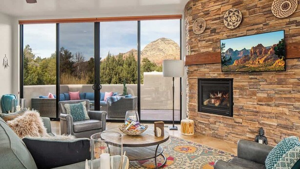 Un salón amplio con pared de piedra, chimenea y ventana grande con vistas a un paisaje montañoso.