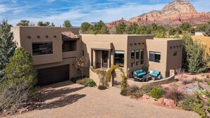 Una casa moderna con garaje, un patio con mobiliario exterior y vista a formaciones rocosas rojas en el fondo.