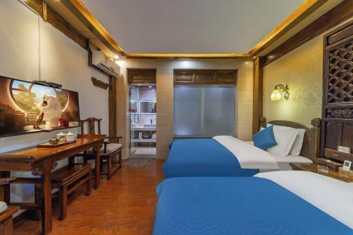 A hotel room with two beds, a wooden desk, a television, and a view of a kitchen area.
