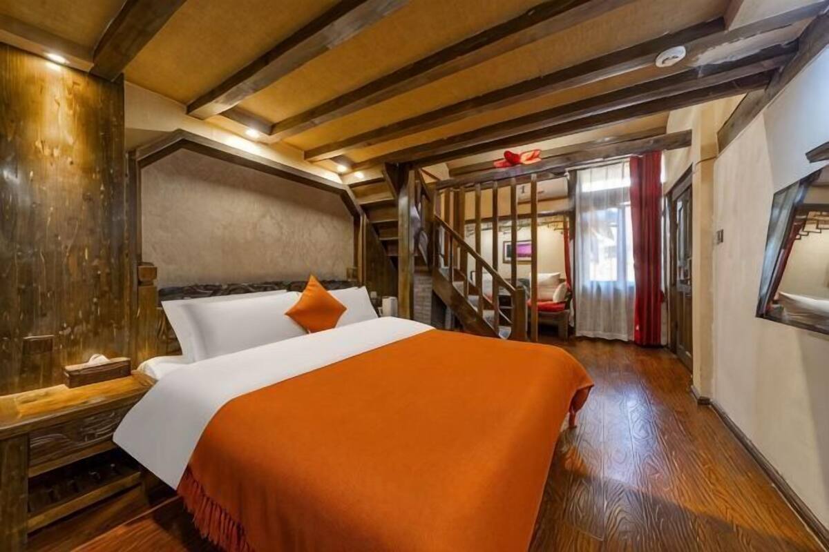 A room with a bed, wooden beams, a staircase, and a view of the outside.