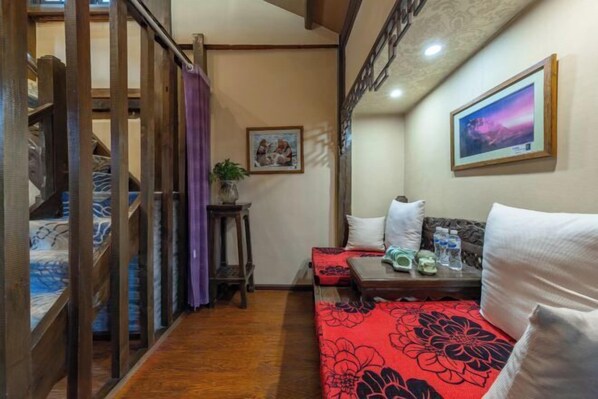 A narrow hallway with a wooden staircase, a sofa with a red floral cover, a small table with water bottles, and a framed picture on the wall. - Lijiang Sifang Inn (Lijiang)
