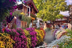 A traditional wooden building with a staircase and balconies, surrounded by vibrant flowers and a small stream. - Lijiang Sifang Inn (Lijiang)