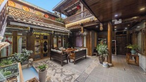 Un edificio de madera tradicional con un patio, que incluye una mesa y sillas de madera, plantas en macetas y una entrada decorativa.