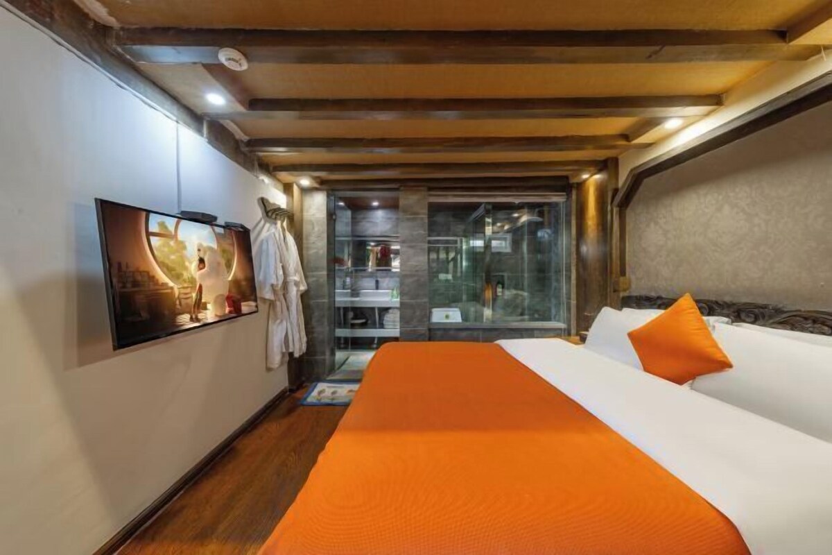 A hotel room with a large bed, a television, and a glass door leading to a bathroom.