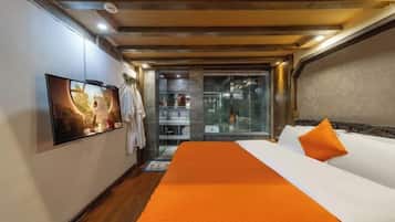 Quarto de hotel com uma cama grande, televisão e porta de vidro para um banheiro.