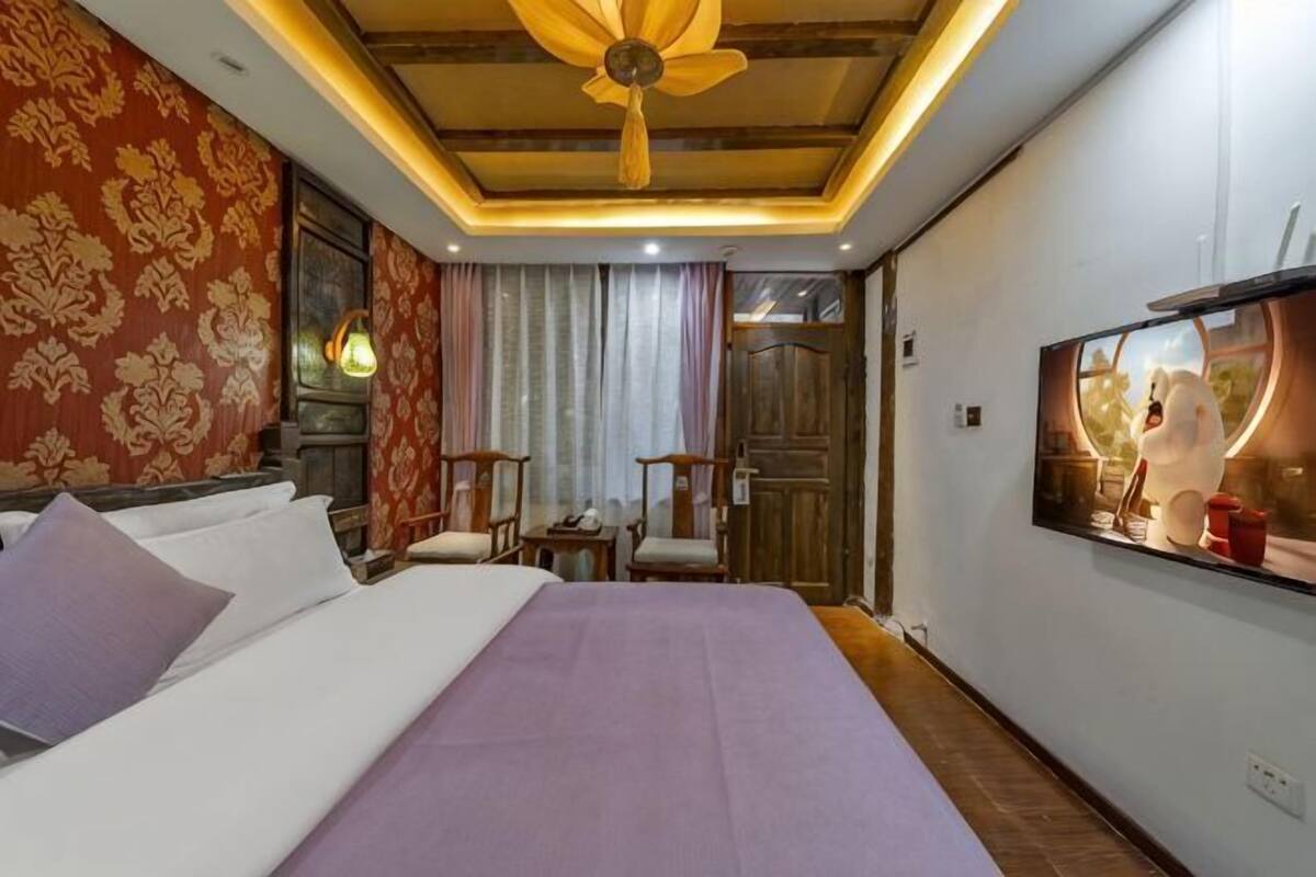 A hotel room with a bed, a desk, a chair, a television, and a ceiling fan.