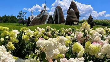Um jardim com diversas flores e uma estrutura arquitetônica única com telhado pontiagudo.