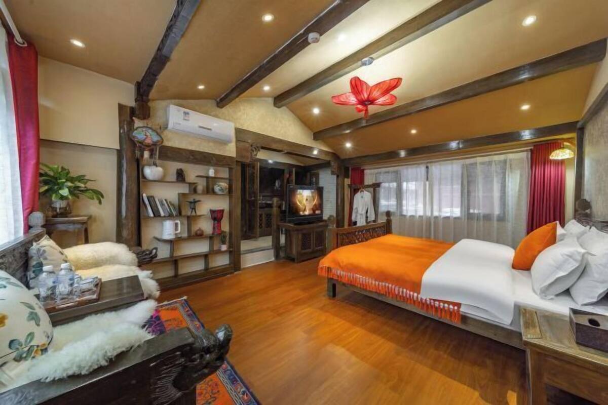 A spacious room with a large bed, wooden beams, a ceiling flower light, and a bookshelf with various items.