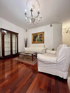 A living room with a white sofa, a glass-top coffee table, a wooden cabinet, and a chandelier. - Cozy and quiet apartment in the city center (Napoli)
