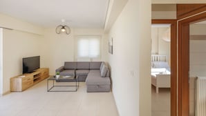 A modern living room with a sectional sofa, a TV on a wooden entertainment unit, and a coffee table. - Urban Oasis with Acropolis Views by GHH (Kallithea)