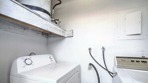 A laundry room with a front-loading washer and dryer, a wooden shelf above the washer, and a wall-mounted electrical box. - Your Vegas Home From Home! Sleeps 6! (Las Vegas)