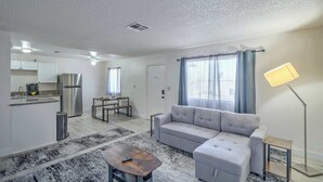 A modern living room with a sofa, a coffee table, a lamp, and a kitchen area with a refrigerator and cabinets. - Your Vegas Home From Home! Sleeps 6! (Las Vegas)