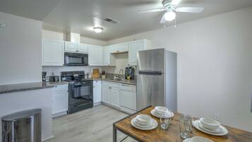 A modern kitchen with white cabinets, stainless steel appliances, a dining table set with plates and glasses, and a ceiling fan.