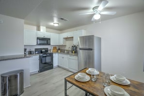 A modern kitchen with white cabinets, stainless steel appliances, a dining table set with plates and glasses, and a ceiling fan.