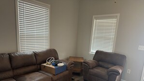 Een woonkamer met een bruine leren bank, een bruine fauteuil en een houten bijzettafeltje met een doos en een lamp.