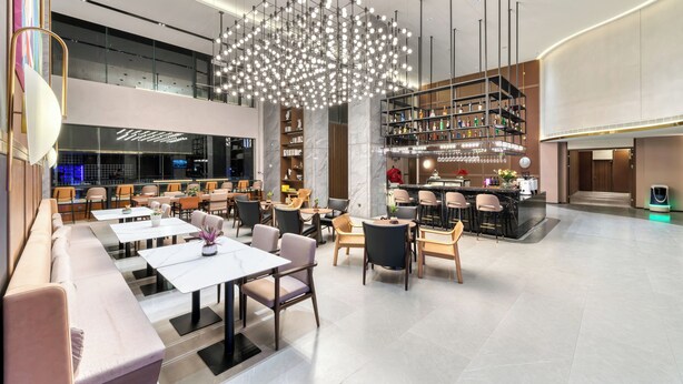 En modern hotellobby med sittgrupper, en bar och en stor kristallkrona.