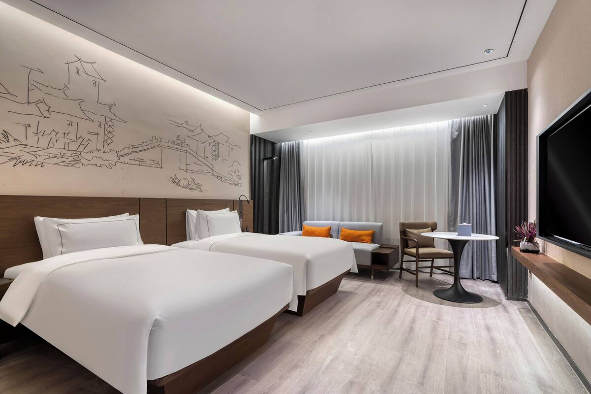 A hotel room with two beds, a seating area with a table, and a large TV.
