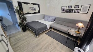 Een moderne slaapkamer met een bed, bank en een klein tafeltje met een lamp. Er hangen afbeeldingen in lijsten aan de muur en staat een potplant.