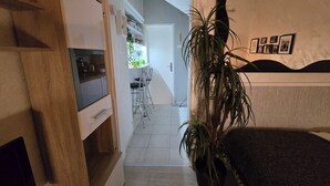 Een hal die leidt naar een keuken met een eethoek, een grote potplant en een bed met hoofdeinde.